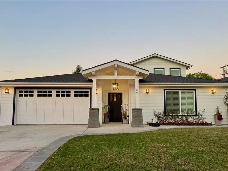 White craftsman-style home with a gabled entry porch, stone column bases and a carriage-style double garage at dusk at 144 Via La Circula, Redondo Beach, California
